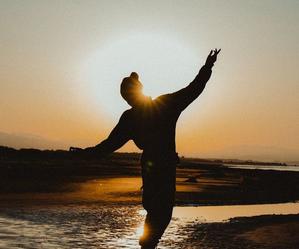 A person balancing in a simple yoga stance outdoors at sunrise.